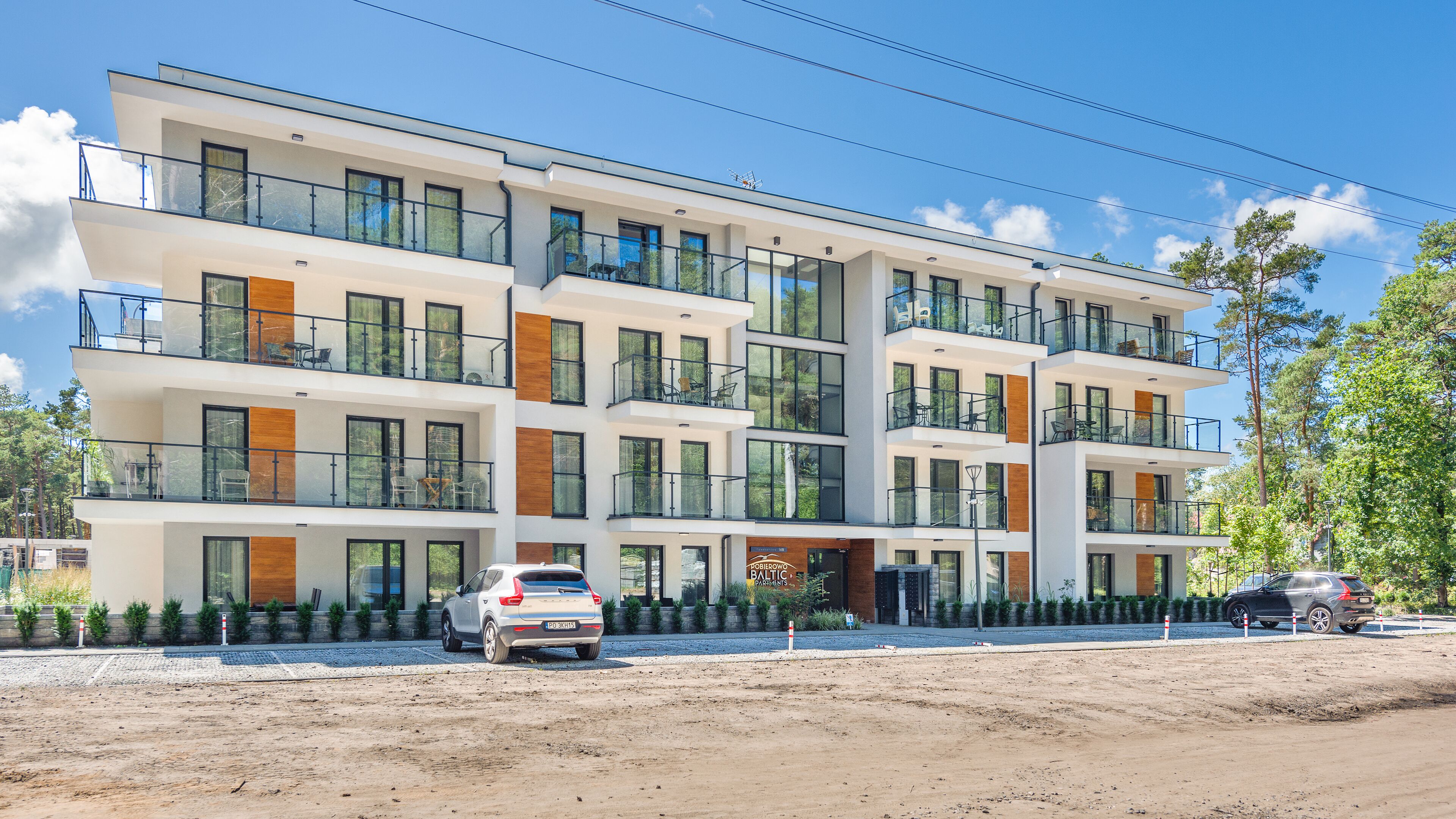 A multi-story residential building with balconies, large windows, and a parking area.