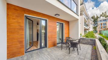 A modern apartment with a wooden facade, large sliding glass doors, and a patio with outdoor furniture.