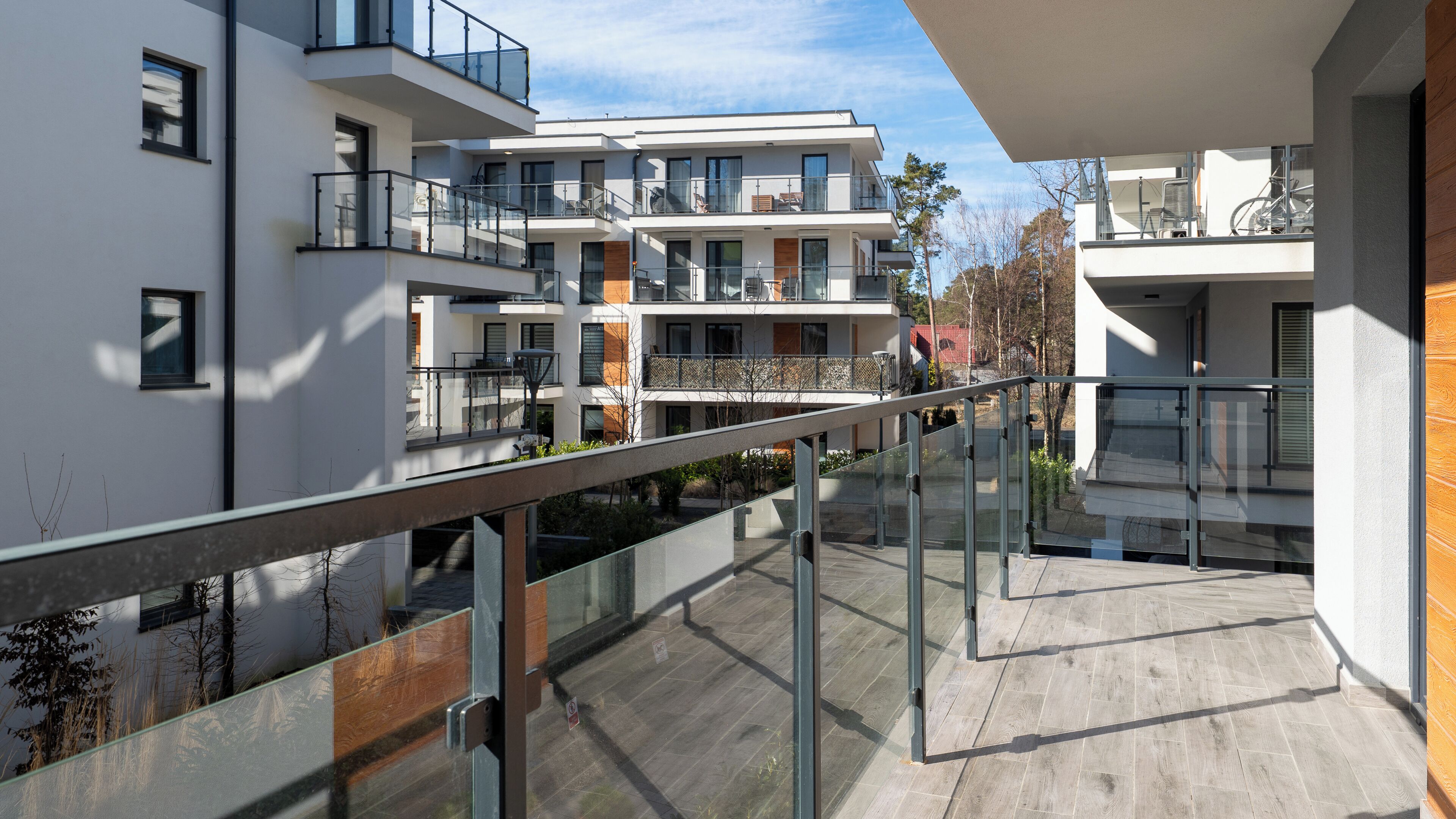 Un moderno edificio residencial de varios pisos con balcones, una terraza de madera y una vista despejada del entorno.