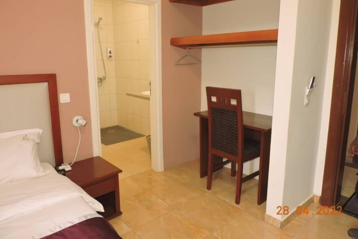A hotel room with a bed, a wooden chair, a desk, and a shower area.