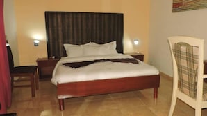 A hotel room with a bed, two bedside tables, a chair, and a wall-mounted artwork. - IRIS HOTEL (Yaoundé)