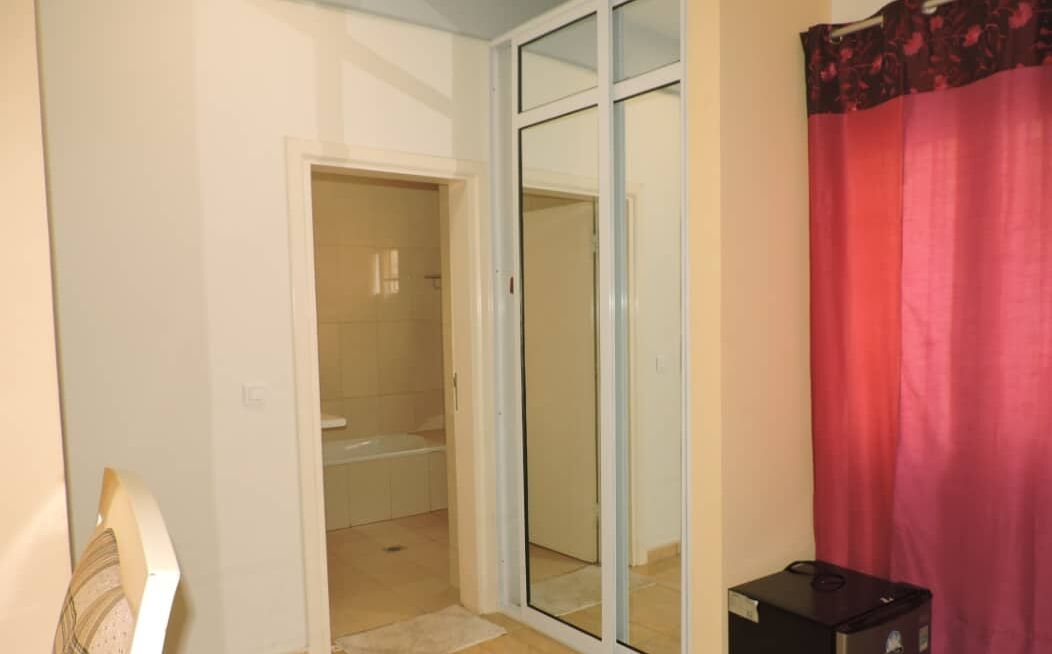 A room with a sliding glass door leading to a bathroom, a small table, and a red curtain.