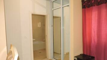 A room with a sliding glass door leading to a bathroom, a small table, and a red curtain.
