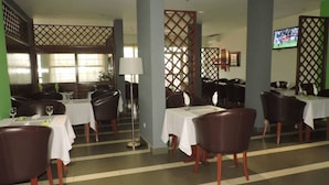 A restaurant with tables set for dining, a TV screen, and a decorative partition. - IRIS HOTEL (Yaoundé)
