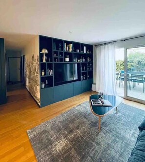A modern living room with a dark blue entertainment unit, a wooden coffee table, and a large window with a view of the outdoors.