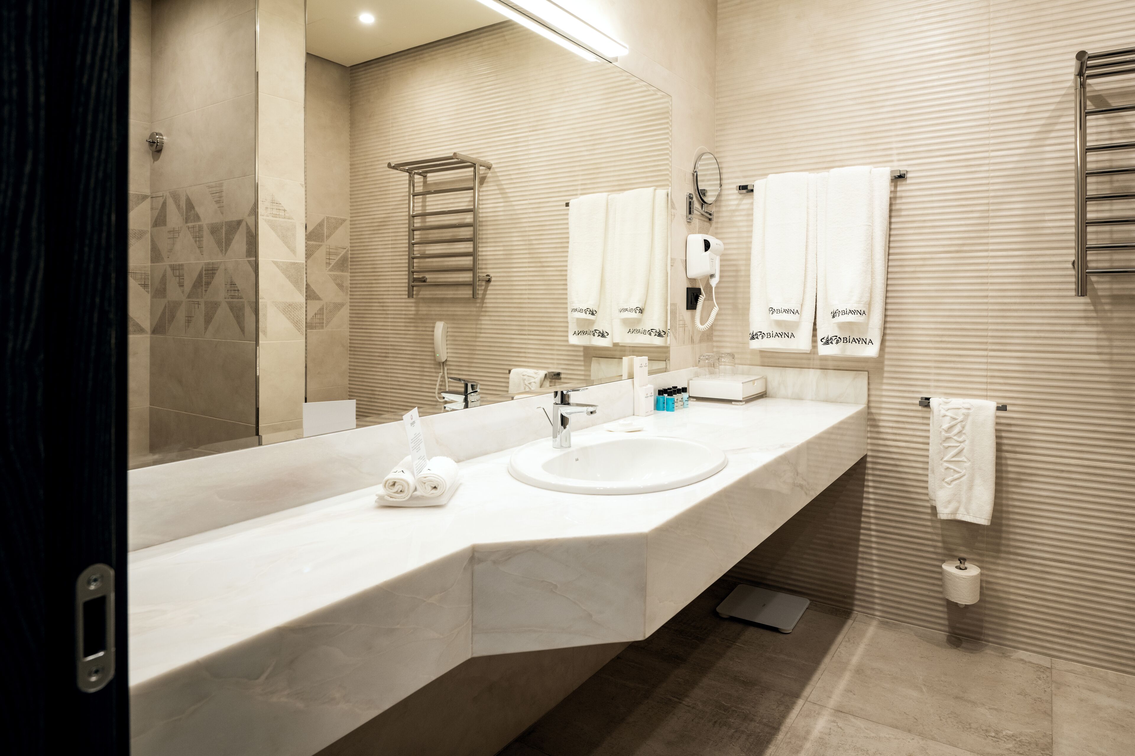 Un bagno moderno con un lavandino ampio, uno specchio, un porta asciugamani e un termosifone per asciugamani.