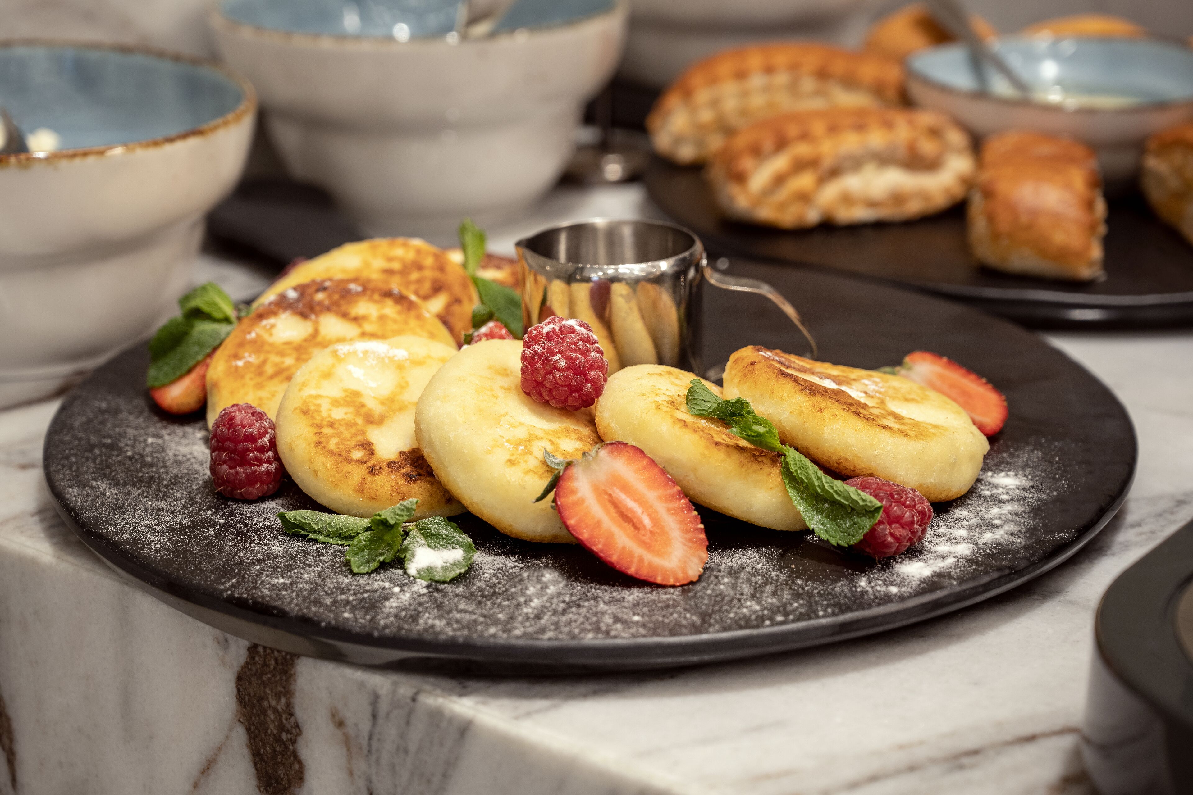 Un plato de postre con panqueques, fresas y frambuesas sobre una superficie de mármol.