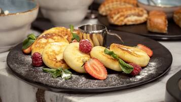 Un plato de postre con panqueques, fresas y frambuesas sobre una superficie de mármol.