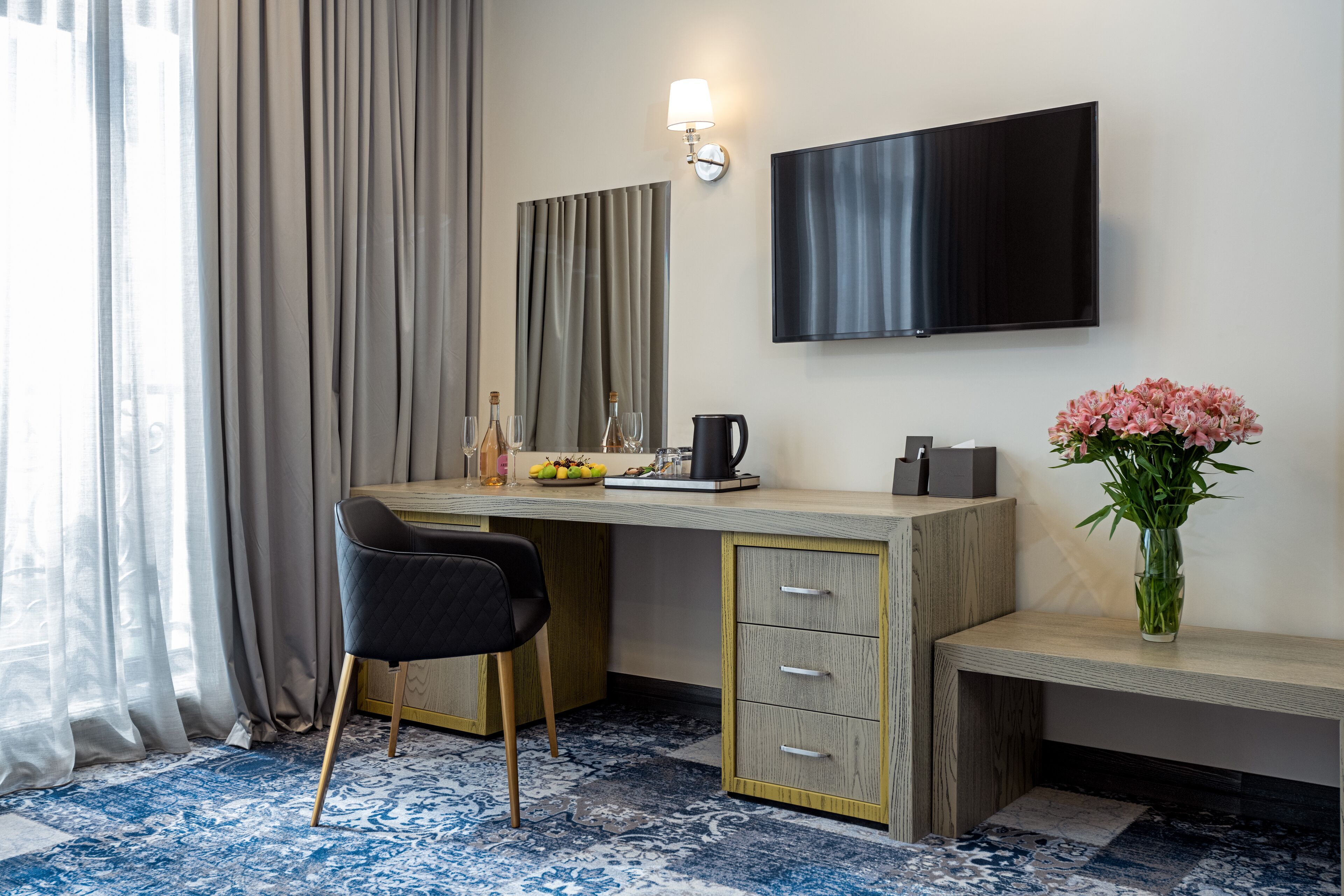 Et hotelværelse med skrivebord, stol, fjernsyn og en vase med blomster.