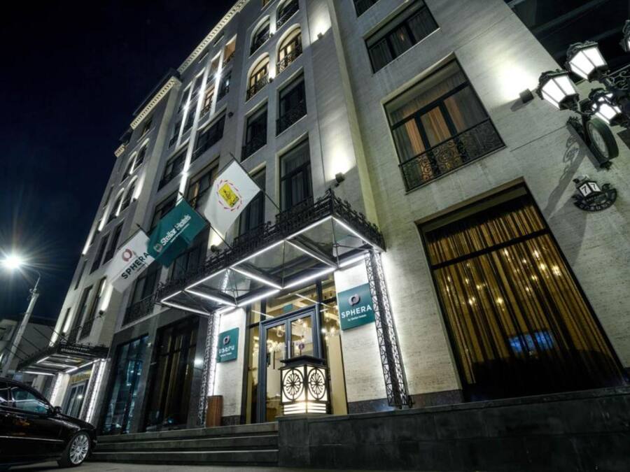 A multi-story hotel with a modern facade, illuminated signage, and a prominent entrance with a glass door.