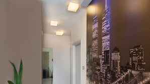 A hallway with a cityscape mural, recessed lighting, and a potted plant. - ALINA HOUSE (Ialysos)