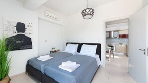 A modern bedroom with two beds, a kitchen in the background, and a decorative wall piece. - ALINA HOUSE (Ialysos)