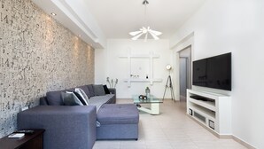 A modern living room with a sectional sofa, a glass coffee table, a flat-screen TV, and a decorative wall with abstract patterns. - ALINA HOUSE (Ialysos)