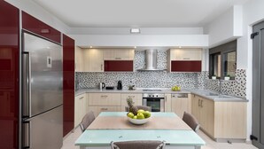 A modern kitchen with stainless steel appliances, a dining table with chairs, and a fruit bowl. - ALINA HOUSE (Ialysos)