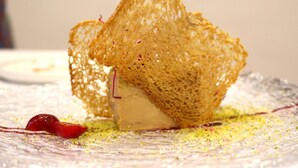 Un postre con una estructura crujiente y similar a enrejado sobre un plato de diseño decorativo.