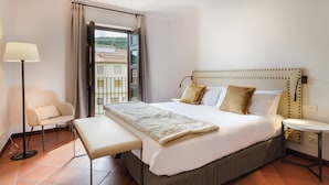 A hotel room with a bed, bedside table, lamp, chair, and an open window with a view of buildings. - Hotel Palacio Matutano Daudén (La Iglesuela del Cid)