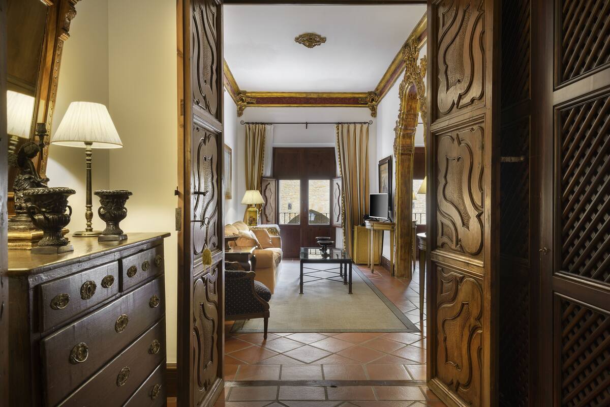 A hallway with ornate wooden doors, a sofa, a coffee table, and a television in a room.