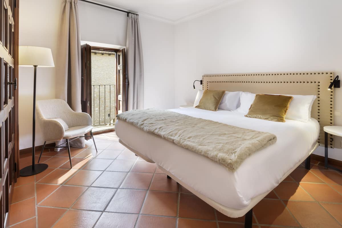 A hotel room with a large bed, a chair, a lamp, and a view of the outside.