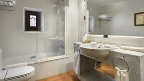 Un baño moderno con ducha de vidrio, inodoro blanco y lavamanos de mármol con un espejo grande.