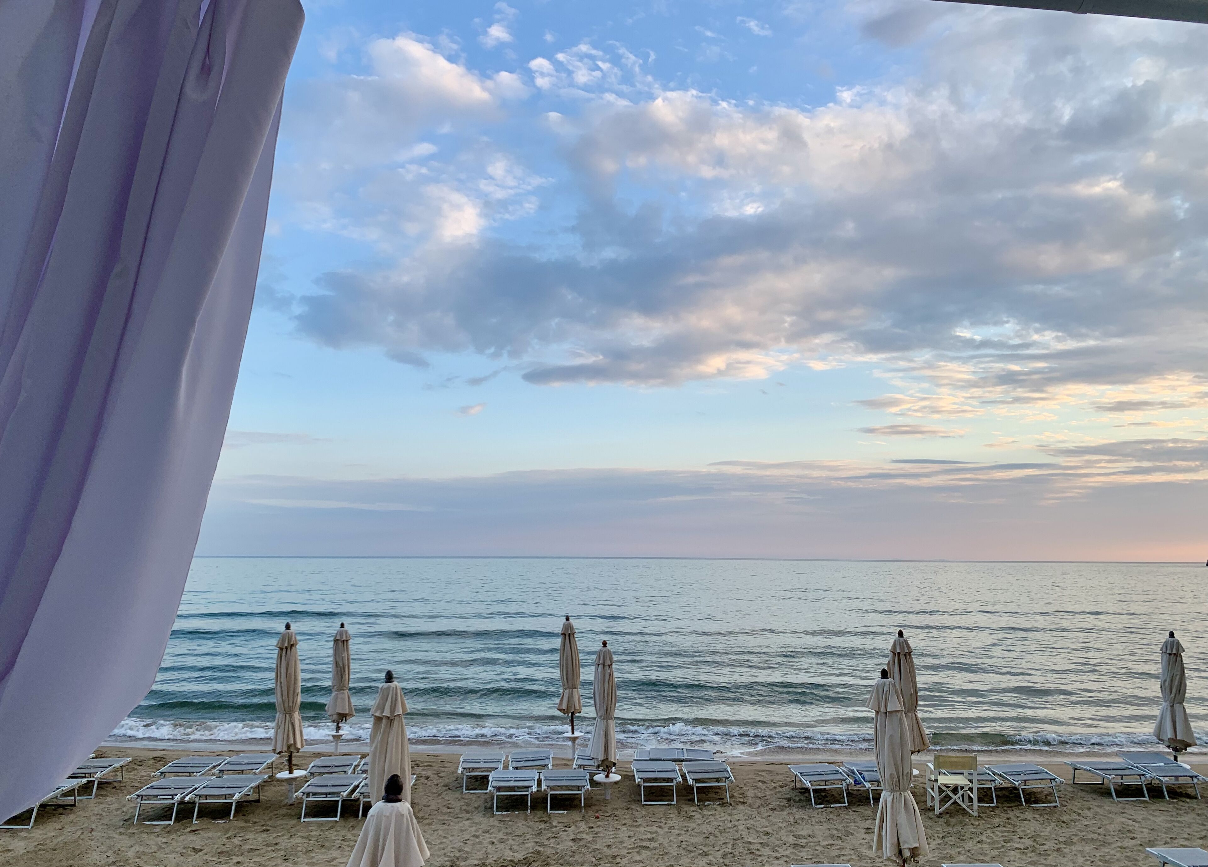 A beach with sun loungers and umbrellas, a clear sky, and the ocean.