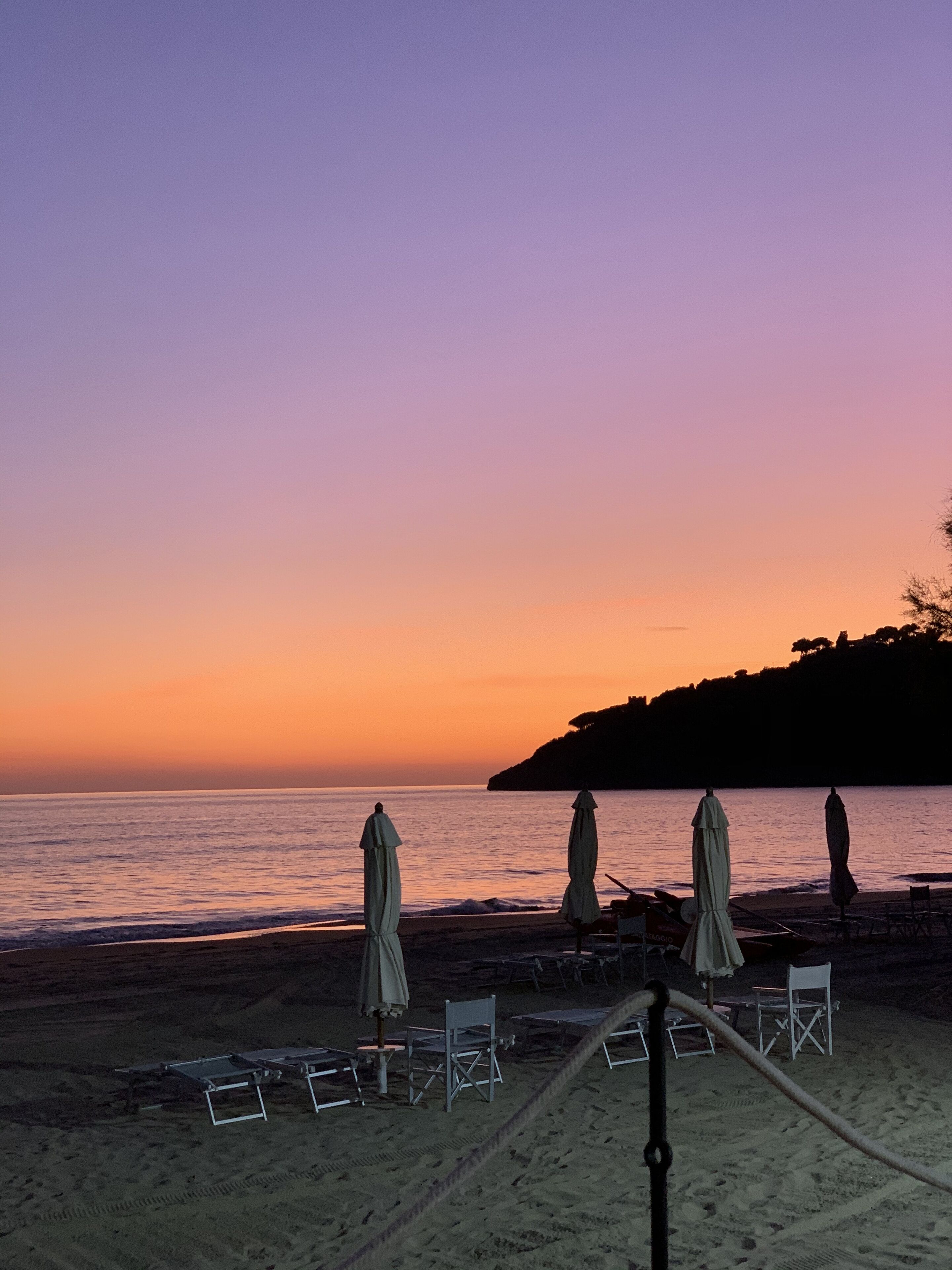 A beach with umbrellas and chairs, a clear sky, and a calm sea.