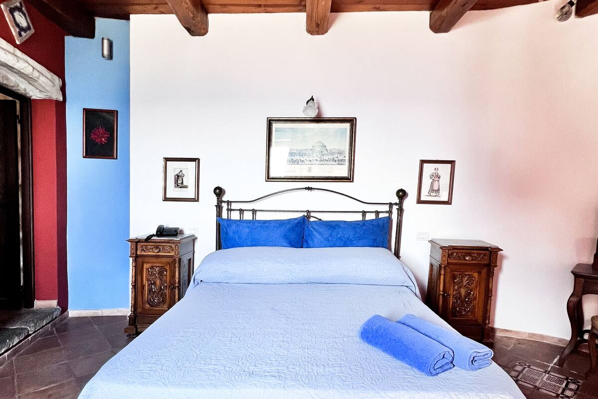 A bedroom with a bed, wooden headboard, two nightstands, a framed picture on the wall, and a tiled floor.
