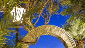 An outdoor dining area with a stone archway, palm trees, and a view of the sea. - Aeneas' Landing Resort (Gaeta)