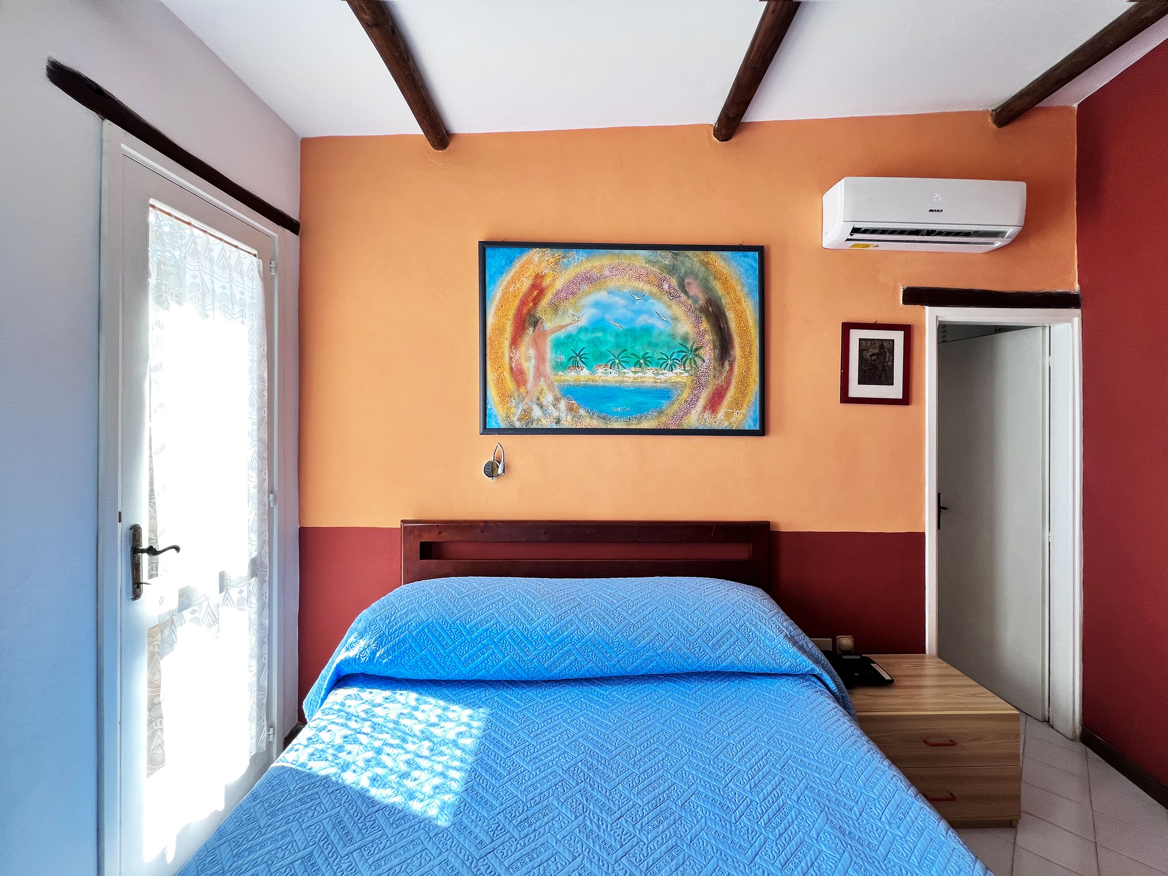 Une chambre à coucher avec un lit, un tableau, un appareil de climatisation et une porte.
