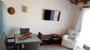 Uma sala de jantar com uma mesa e cadeiras, um sofá e uma televisão na parede.