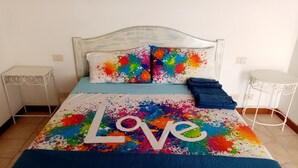 Cama com colcha colorida exibindo a palavra 'Love' e respingos de tinta.