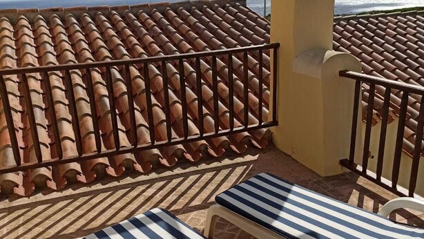 Um terraço com chão em azulejos, duas cadeiras de descanso listradas e vista para o mar.