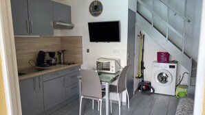 Een kleine keuken met een magnetron, broodrooster en koffiezetapparaat. Er staat een eettafel met stoelen in de buurt van de keuken. Een wasmachine is in de hoek te zien.