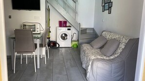 Een knus woongedeelte met een bank, een eettafel met stoelen, een wasmachine en een trap.