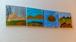 Une série de quatre tableaux représentant des paysages, exposés sur un mur à texture.