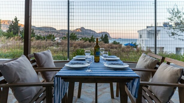 Un espace de restauration en plein air avec une table dressée pour deux personnes, entouré de chaises en bois dotées de coussins, offrant une vue sur un paysage pittoresque.