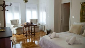 A hotel room with a wooden floor, a bed with white linens, a small table with a chessboard, two chairs, and a large window with blinds. - THE VILLAR HOUSE (Estación de Brazatortas-Veredas)