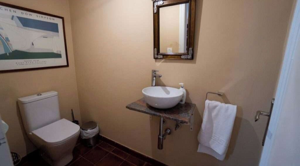 A bathroom with a toilet, sink, mirror, and towel rack.