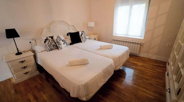 A double room with two beds, bedside tables with lamps, a radiator, and a window.