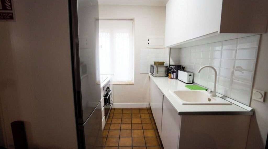 Una cocina compacta con armarios blancos, microondas, tostadora y pileta.