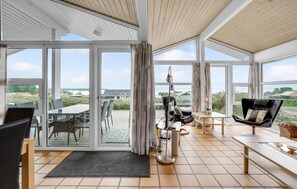 A spacious living area with a large sliding glass door leading to an outdoor patio. Inside, there is a dining table with chairs, a sofa, and a small side table. - Amazing home in Sjølund with kitchen (Sjølund)
