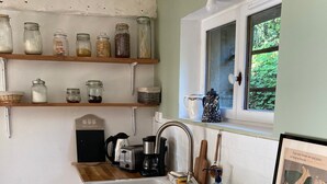 A kitchen with a wooden countertop, a sink, a stove, and shelves with jars.