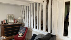 A living room with a red armchair, a sofa, a wooden dresser, and a window with white wooden shutters.