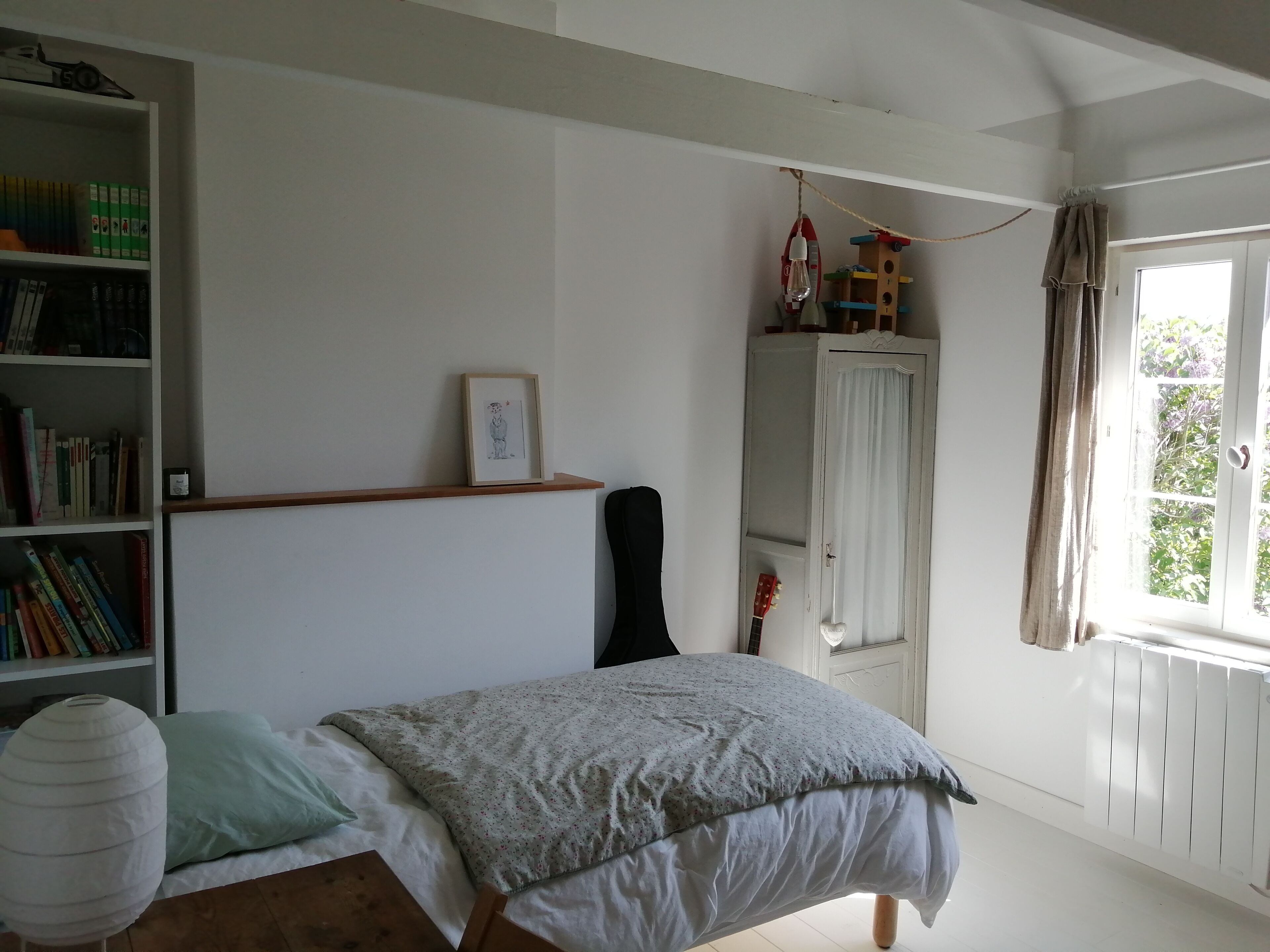A bedroom with a bed, a bookshelf, a wardrobe, and a window with curtains.