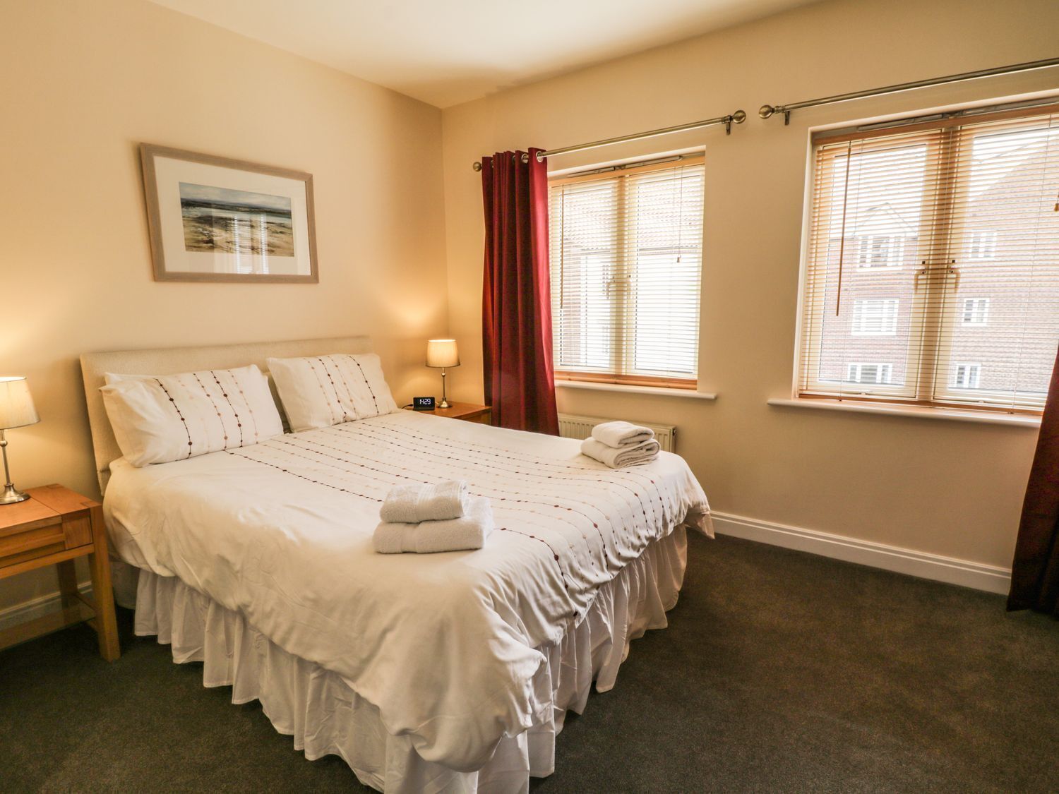 Habitación de hotel con una cama grande, una mesita de noche con lámpara, una ventana con cortinas y un cuadro en la pared.
