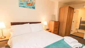 Ett hotellrum med en stor säng, två sängbord, ett litet bord, en garderob i trä, ett badrum med en handduksställning och en tavla på väggen.
