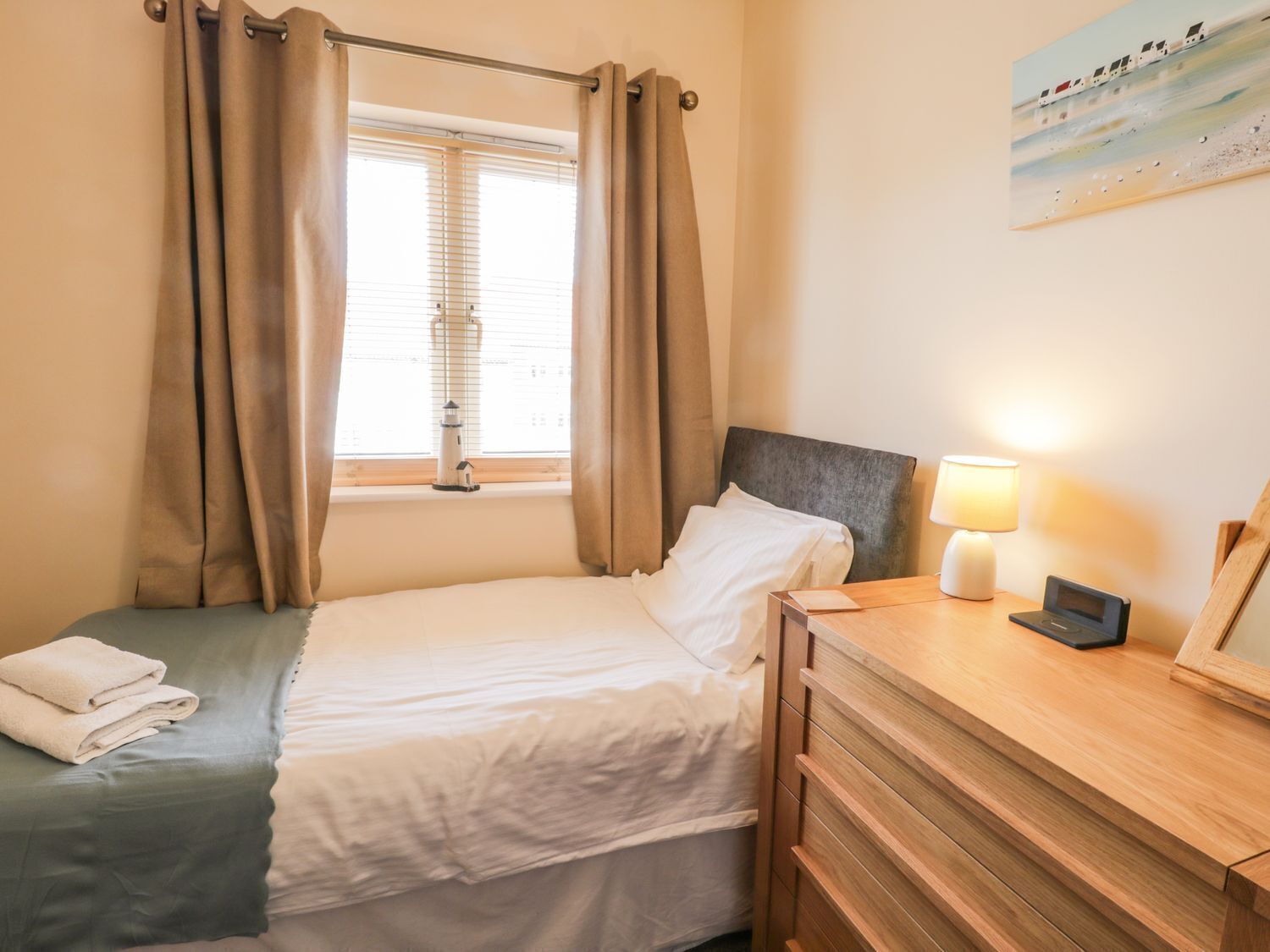 A neatly made bed with white linens, a bedside table with a lamp, and a window with curtains.