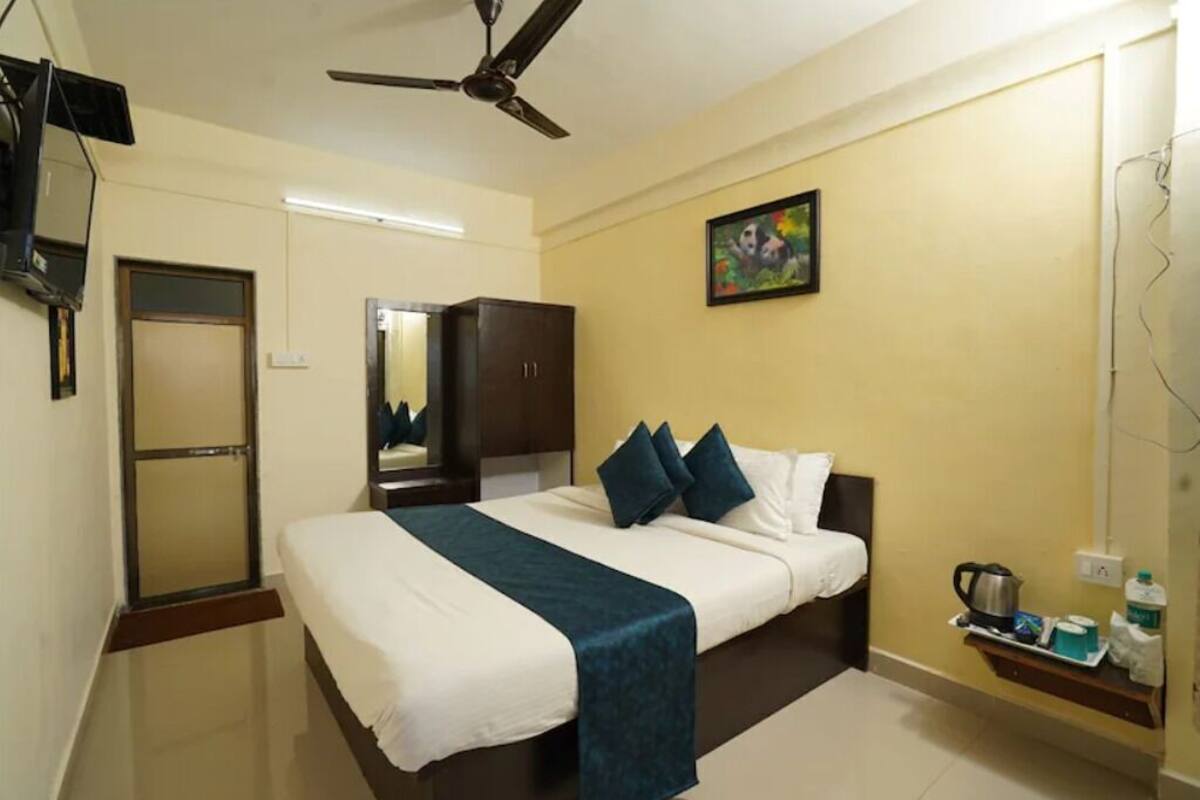 A hotel room with a bed, a ceiling fan, a mirror, a painting, and a small shelf with toiletries.