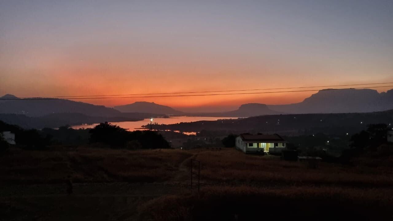 Ländliche Landschaft im Abendlicht, mit einem Haus im Vordergrund und Bergen im Hintergrund.