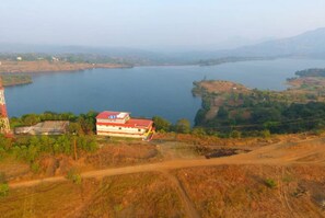 A large body of water with a building featuring a red roof and white walls, surrounded by dry, hilly terrain. - Hilltop Retreat (Pune)