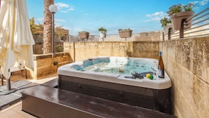 A hot tub with a stone wall backdrop, surrounded by potted plants and a white umbrella. - Harbour Views Gozitan Villa + Shared Pool (Ghajnsielem)